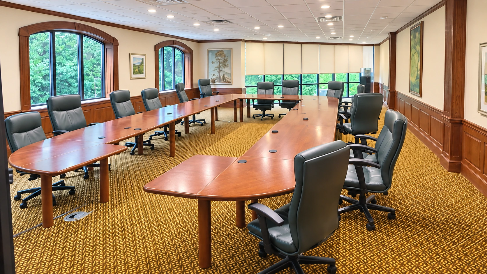 Wide view of the shared executive boardroom with U-shaped meeting tables, chairs and windows overlooking the grounds.