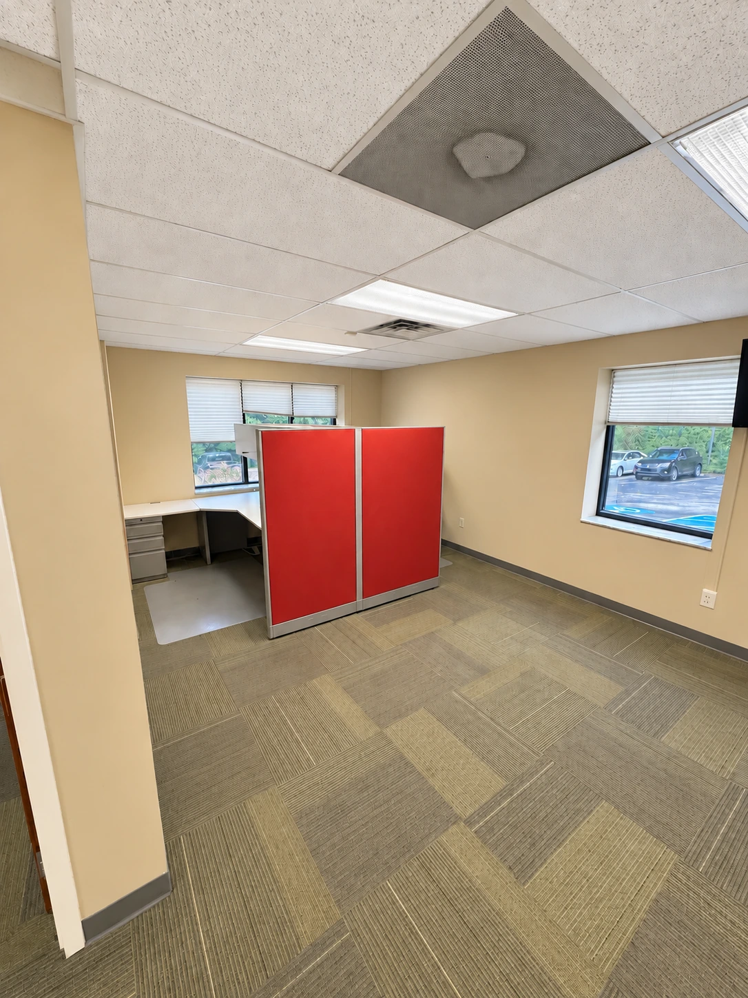 Open work area with red cubicle partitions, existing work surfaces and windows on two walls.