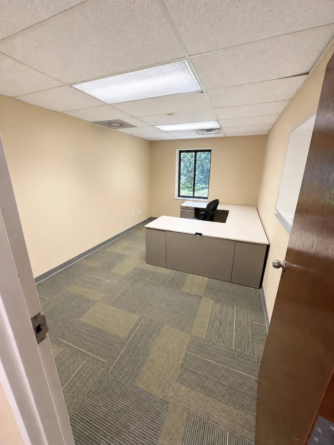 Private office with an existing desk, office chair, window and whiteboard.