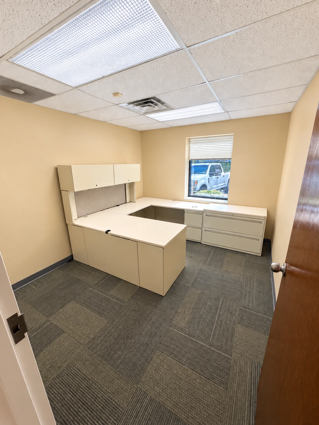 Private office with a wraparound work surface, overhead storage and a window.