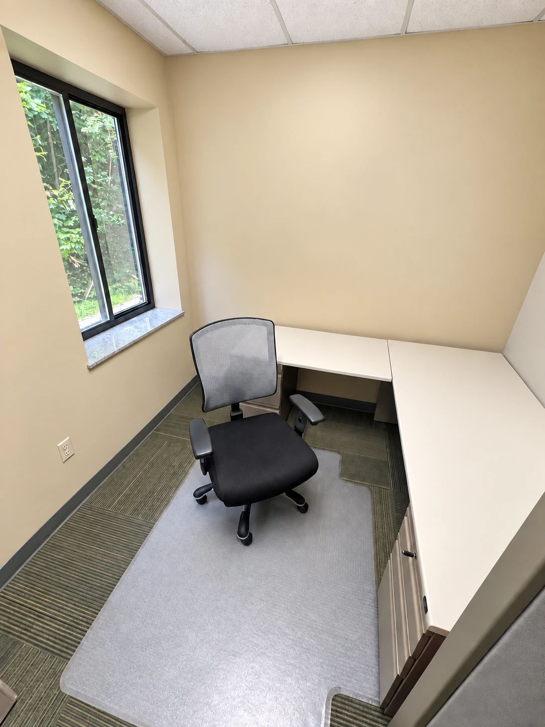 Windowed private office with a corner workstation and an office chair.