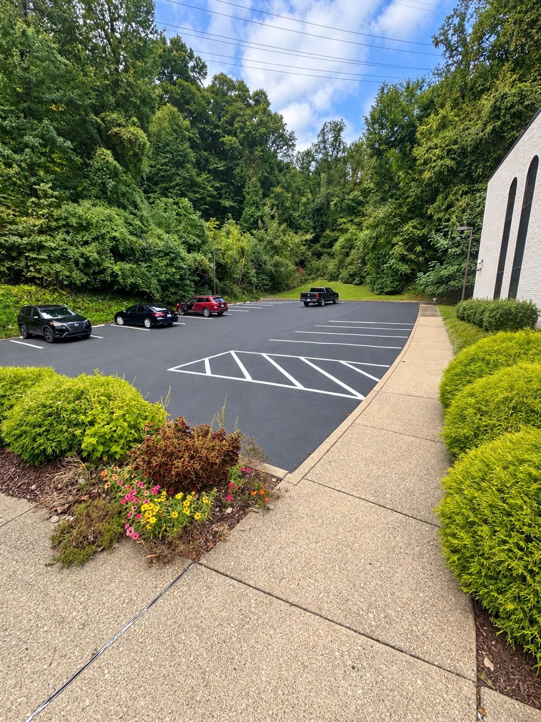Shared on-site parking beside the building, with striped spaces, landscaped beds and a pedestrian walkway.