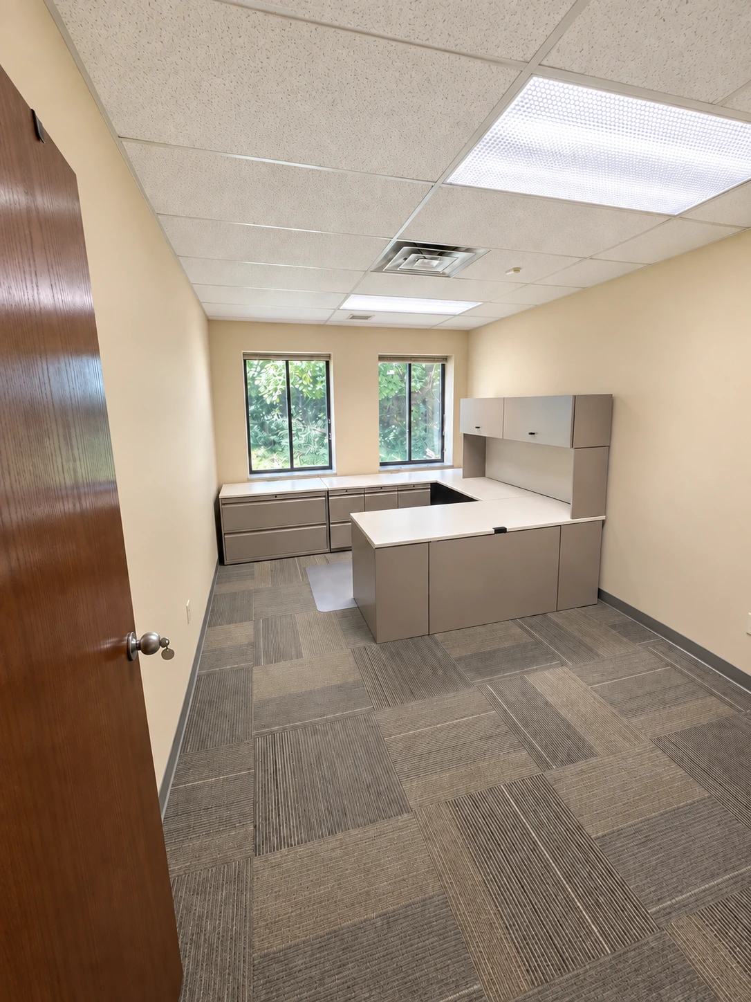 Windowed private office with a wraparound desk and overhead storage.